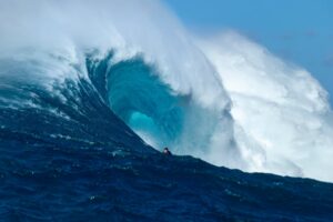 Surfer riding a large wave in the ocean with a clear sky.