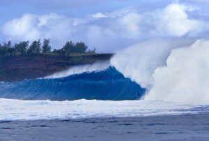 Gorgeus scene with a big ocean blue wave with a  withe foam curling over surfer with a beautiful clif and sy in background
