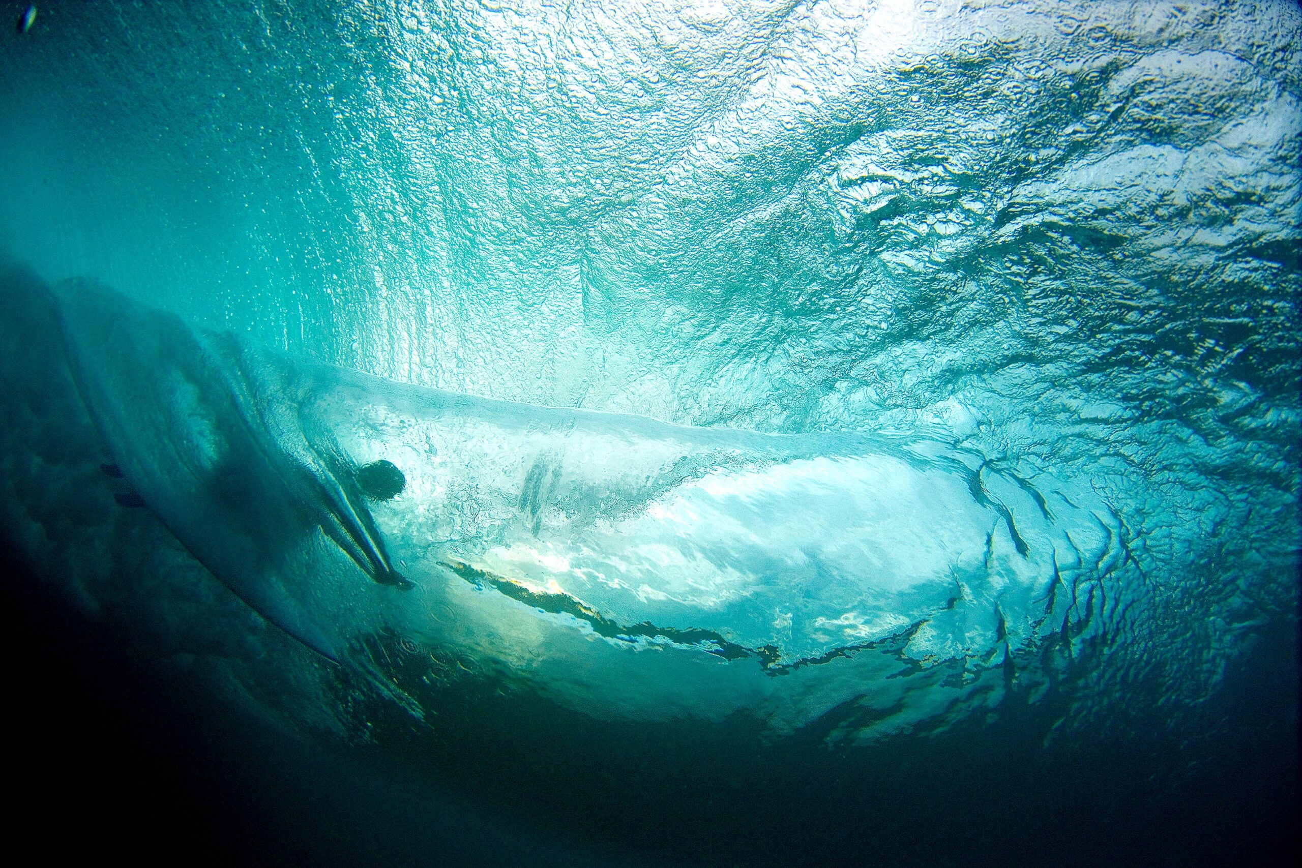 Underwater view of a surfer riding a wave with sunlight filtering through the water.
