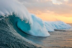 Turquoise big ocean wave with colored sky in background
