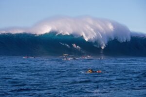 Surfers waiting for waves in the ocean with a large wave in the background