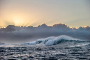Ocean waves crashing against a sunset sky with clouds