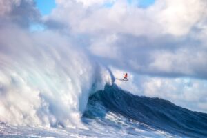 Person surfing a large wave with a dramatic sky
