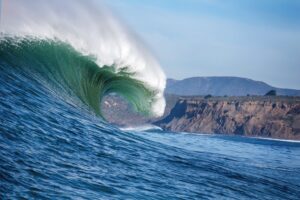Large ocean Mavericks wave curling over itself with a mountainous landscape in the background.
