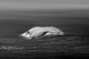 Black and white photo of a surfer riding a large wave in the ocean.