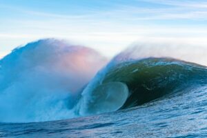 Large wave crashing in the ocean with a clear sky.