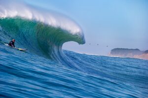Surfer riding a large wave with a clear sky in the background