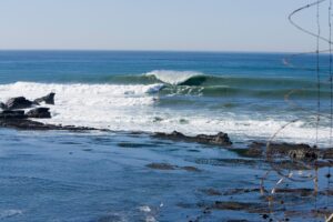 Ocean waves Mavericks crashing against rocks with a clear sky