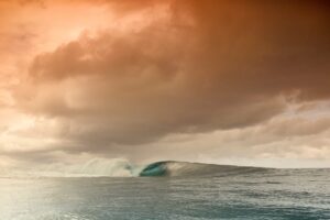 Wave crashing in the ocean under a dramatic sky with clouds.