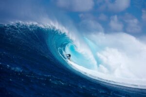 Surfer riding a large wave in the ocean with a blue sky.
