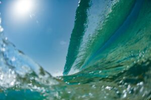 Close-up of a breaking wave with sunlight and blue sky.