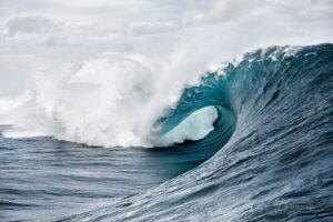 Large ocean wave with white foam curling over itself against a cloudy sky.