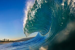 Close-up of a breaking big wave with clear blue sky and beach in the background