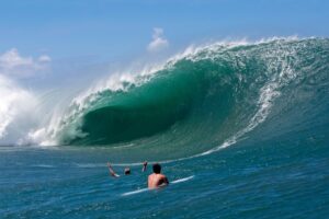 Two surfers riding a large wave in the ocean with a clear blue sky.