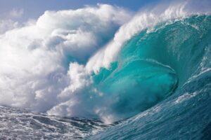 A big large ocean wave with white foam against a blue sky curling, its ineffable.