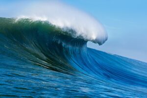Large big ocean wave Mavericks with white foam against a clear blue sky