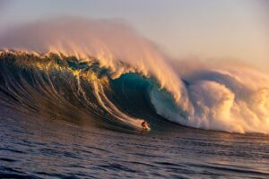 Surfer riding a large wave in the ocean with a sunset or sunrise sky.