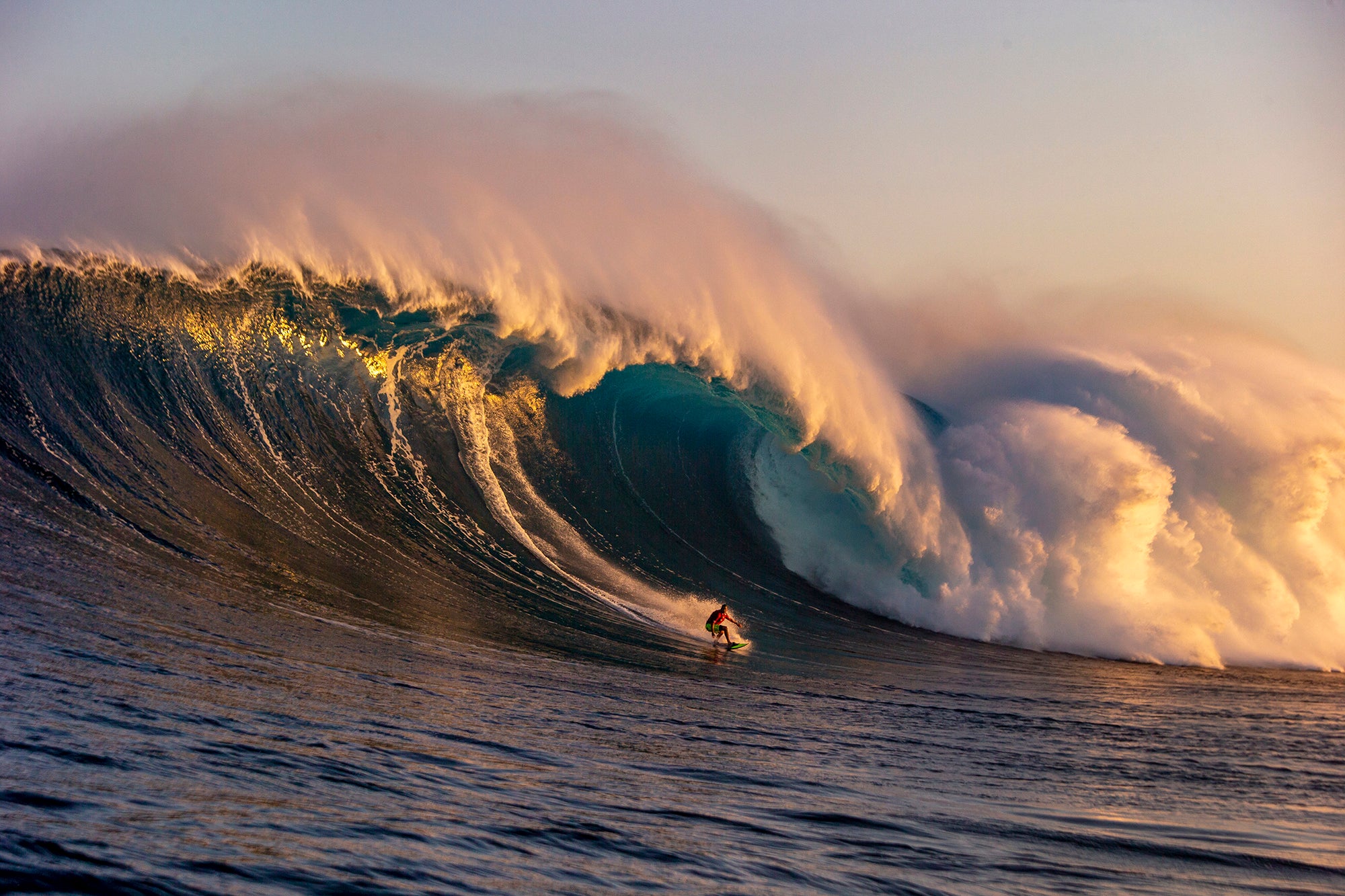 Surfer riding a large wave in the ocean with a sunset or sunrise sky.